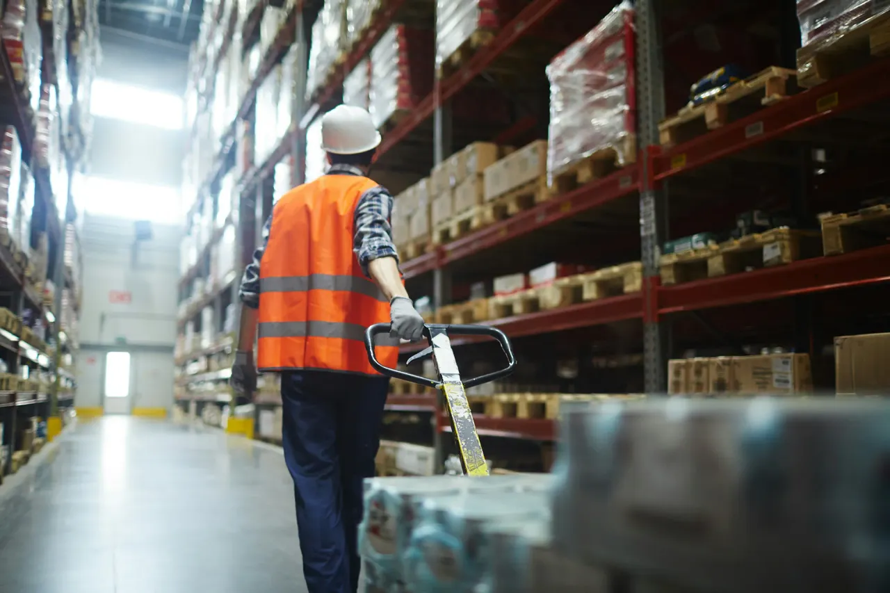 A worker pulls a pallet with packaged items across a warehouse